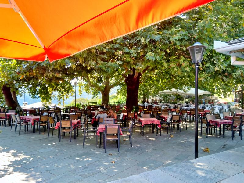 Visitors enjoy their drink and food under the shade of the plane trees in the village square